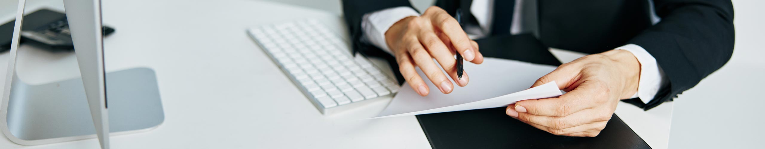 Geschäftsmann am Computer mit Blatt und Kugelschreiber in der Hand
